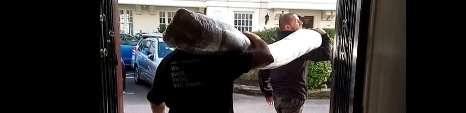 Two removal workers carrying a rolled rug, with workwear lettering visible